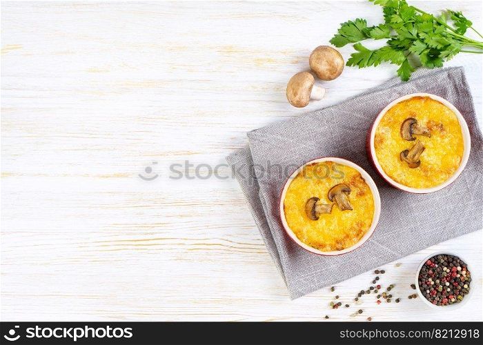Chicken and mushroom casserole with golden crust, julienne with baked cheese, creamy gratin in portion ramekin clay pot on white wooden background. French cuisine. Top view, flat lay with copy space. French Julienne casserole with chicken and mushroom in portion ramekin on white background