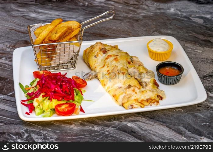 Chicken and mushroom pancakes or crepes with salad and french fries on a white plate