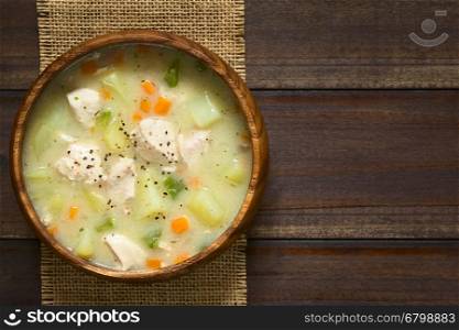 Chicken and potato chowder soup with green bell pepper and carrot in wooden bowl, photographed overhead on dark wood with natural light (Selective Focus, Focus on the soup)