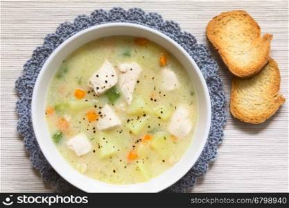 Chicken and potato chowder soup with green bell pepper and carrot in bowl with toasted bread slices on the side, photographed overhead with natural light (Selective Focus, Focus on the top of the soup)