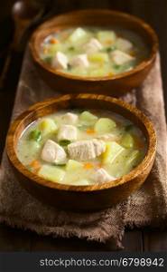 Chicken and potato chowder soup with green bell pepper and carrot in wooden bowls, photographed on dark wood with natural light (Selective Focus, Focus in the middle of the first soup)
