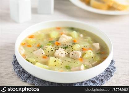 Chicken and potato chowder soup with green bell pepper and carrot in bowl, photographed with natural light (Selective Focus, Focus on the chicken pieces one third into the soup)