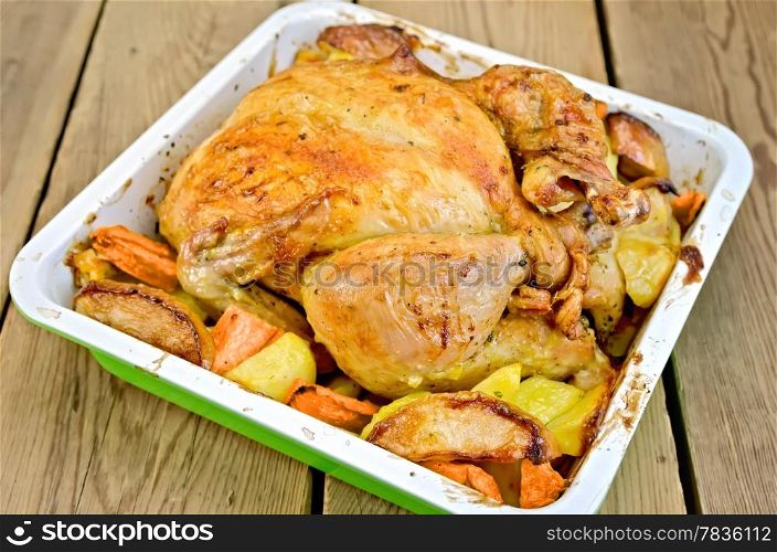 Chicken baked with potatoes, carrots and apples in a tray on the background of wooden boards