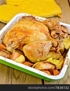 Chicken baked with potatoes, carrots and apples in a tray, potholder on the background of wooden boards