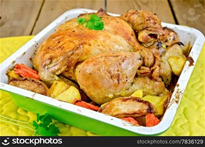 Chicken baked with potatoes, carrots and apples in a tray with parsley, potholder on the background of wooden boards