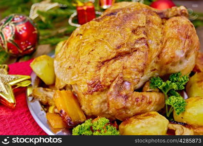 Chicken baked with vegetables and apples on a metal plate, red and gold Christmas toys, napkin, spruce twigs on a wooden boards background