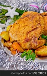 Chicken baked with vegetables and apples on a metal plate, silver toys, fir branches on the background of wooden boards