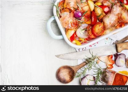 Chicken breast with cut colorful vegetables in enamelled casserole with wooden spoon and kitchen knife on white wooden background, top view, border. Healthy food or diet nutrition concept.