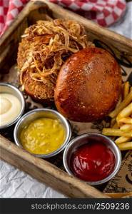 Chicken burger served with french fries and sauces in a wooden case