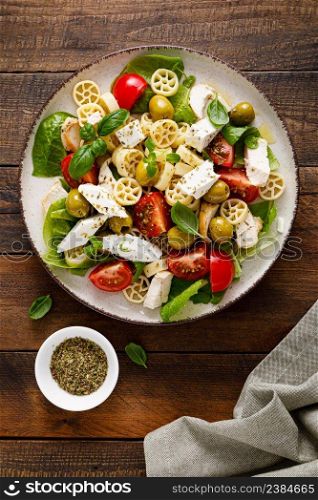 Chicken Caprese pasta salad with mozzarella cheese, olives, tomato and fresh basil. Top view, flat lay