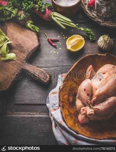 Chicken cooking concept. Raw whole chicken in wooden dish with ingredients on rustic background. Close up