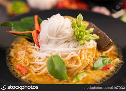 Chicken curry in a black cup with rice noodles, garlic, tomatoes, chilies, and kaffir lime leaves.