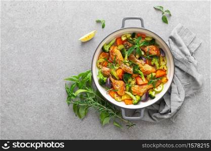 Chicken drumsticks roasted with vegetables in cast iron pan on kitchen table, top down view