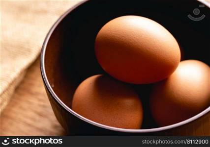 Chicken eggs in brown bowl on wooden table