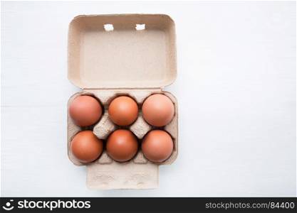 Chicken eggs in egg box on white wooden background.