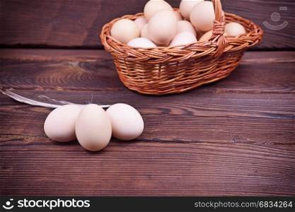 Chicken eggs in shell and in a wicker basket on a brown wooden background