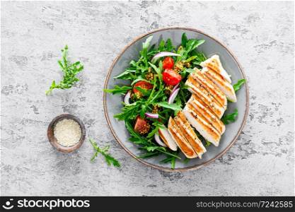Chicken fillet salad with fresh vegetables and arugula. Fresh vegetable salad of arugula, tomatoes, onion and grilled chicken breast.