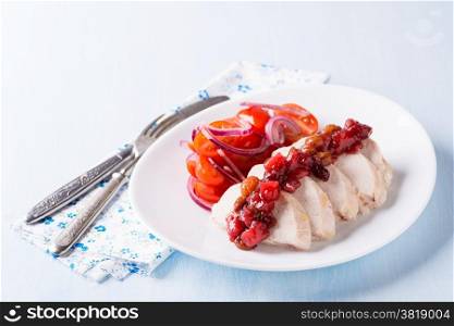 Chicken fillet with cranberry relish and tomato salad, light blue background
