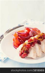 Chicken fillet with cranberry relish and tomato salad, light blue background, closeup. Toned image