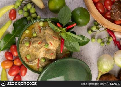 Chicken green curry in a bowl with chilies, basil, eggplant, kaffir lime leaves, and lime