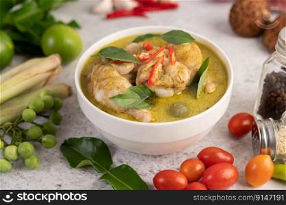 Chicken green curry in a bowl with chilies, basil, eggplant, kaffir lime leaves, and lime