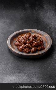 Chicken hearts fried in soy sauce with sa<and sπces in a plate on a textured concrete background