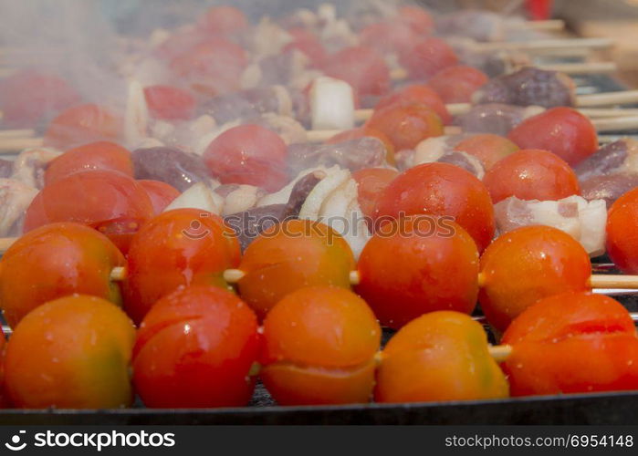 Chicken hearts with tomato and onion cooking on hot grill.