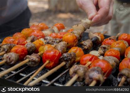 Chicken hearts with tomato and onion cooking on hot grill.