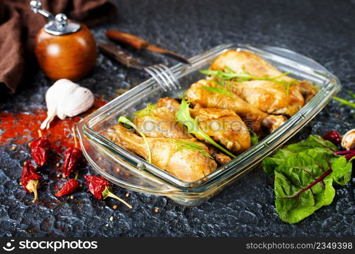chicken legs baked in with fresh garlic and herbal close-up in a baking dish on the table.