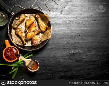 Chicken legs with tomato sauce and green onions. On a black wooden background.. Chicken legs with tomato sauce and green onions.