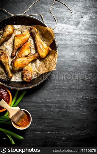 Chicken legs with tomato sauce and green onions. On a black wooden background.. Chicken legs with tomato sauce and green onions.