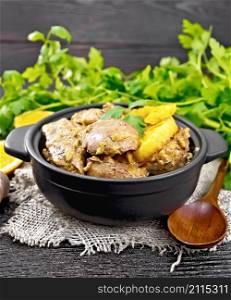 Chicken liver stewed with oranges, sour cream, soy sauce and Provencal herbs in a small pan on burlap, a spoon and parsley on wooden board background
