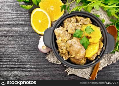 Chicken liver stewed with oranges, sour cream, soy sauce and Provence herbs in a small pan on burlap napkin, spoon and parsley on wooden board background from above
