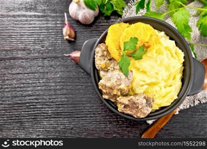 Chicken liver stewed with oranges, sour cream, soy sauce and Provence herbs in a small pan with mashed potatoes on burlap napkin, a spoon and parsley on wooden board background from above