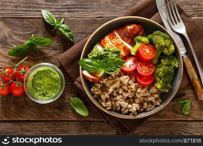 Chicken lunch bowl with broccoli, fresh tomato, pearl barley porridge and basil pesto on wooden rustic background