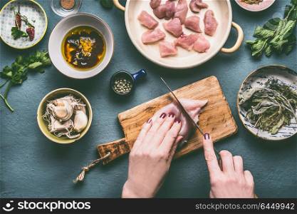 Chicken meal cooking concept. Female hands cutting chicken breast meat on kitchen tables background with bowls , oil , soy sauce and ingredients, top view