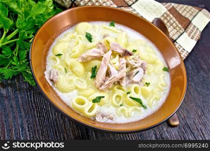 Chicken meat soup, pasta with cream and cilantro in a clay plate, towel, parsley, spoon on a wooden board background