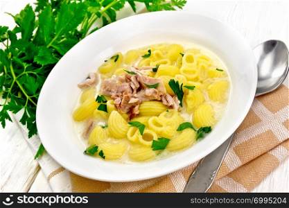 Chicken meat soup, pasta with cream and cilantro in a plate, napkin, parsley, metal spoon on a wooden board background