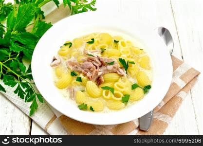 Chicken meat soup, pasta with cream and cilantro in a plate on a towel, parsley, metal spoon on a wooden board background
