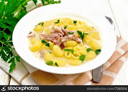 Chicken meat soup, pasta with cream and cilantro in a plate, towel, parsley, metal spoon on a wooden board background