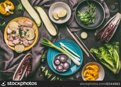 Chicken meat with lemon and vegetables skewers. Grill preparation on kitchen table background with chicken pieces and vegetables in plates and bowls, top view.