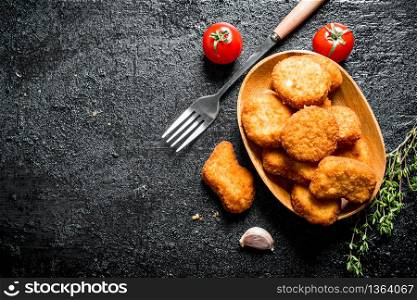 Chicken nuggets in bowl with greens and tomatoes. On black rustic background. Chicken nuggets in bowl with greens and tomatoes.