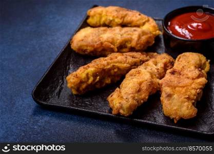 Chicken nuggets with tomato sauce on a concrete background. Copy space. Fried crispy chicken nuggets with ketchup on black plate on a dark background
