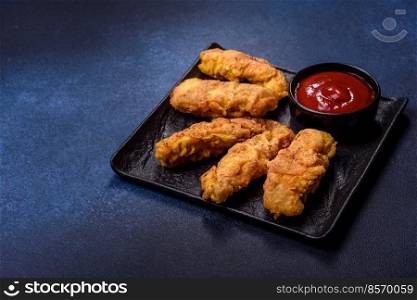 Chicken nuggets with tomato sauce on a concrete background. Copy space. Fried crispy chicken nuggets with ketchup on black plate on a dark background