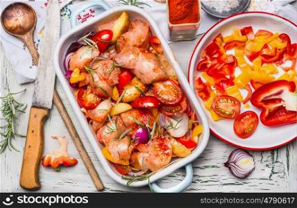 Chicken pieces with cut vegetables and red paprika powder in casserole , on light rustic background with cooking spoon and kitchen knife, top view