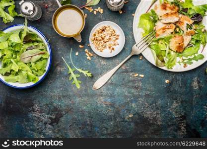 Chicken salad with green mix salad leaves, fork and dressing on rustic background, top view, border. Healthy food and diet eating concept
