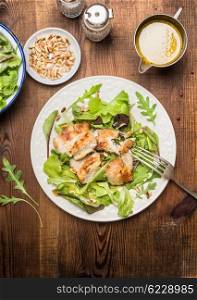 Chicken salad with green salad leaves, pine nuts and olive oil dressing. Healthy diet salad on rustic wooden background, top view. Country chicken salad.