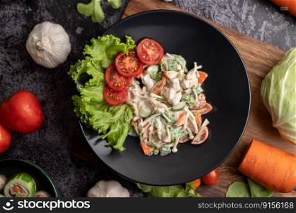 Chicken salad with tomato, needle mushroom, carrots, lettuce and cucumber on a black plate.