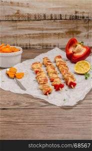 Chicken skewers with peppers, onion and sauteed carrots on the wooden background