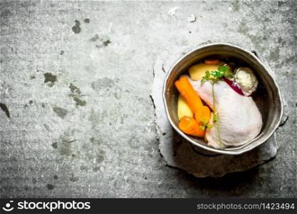 Chicken soup in an old pot with vegetables. On the stone table.. Chicken soup in an old pot with vegetables.